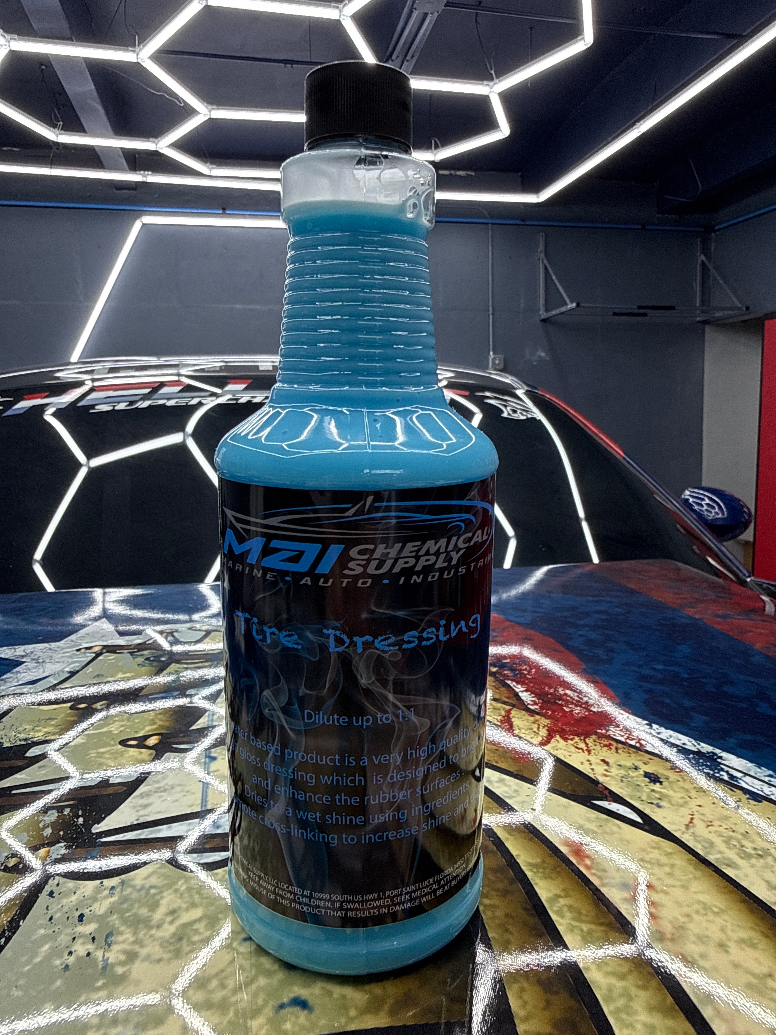 Blue bottle of car care product on a reflective surface with a car in the background