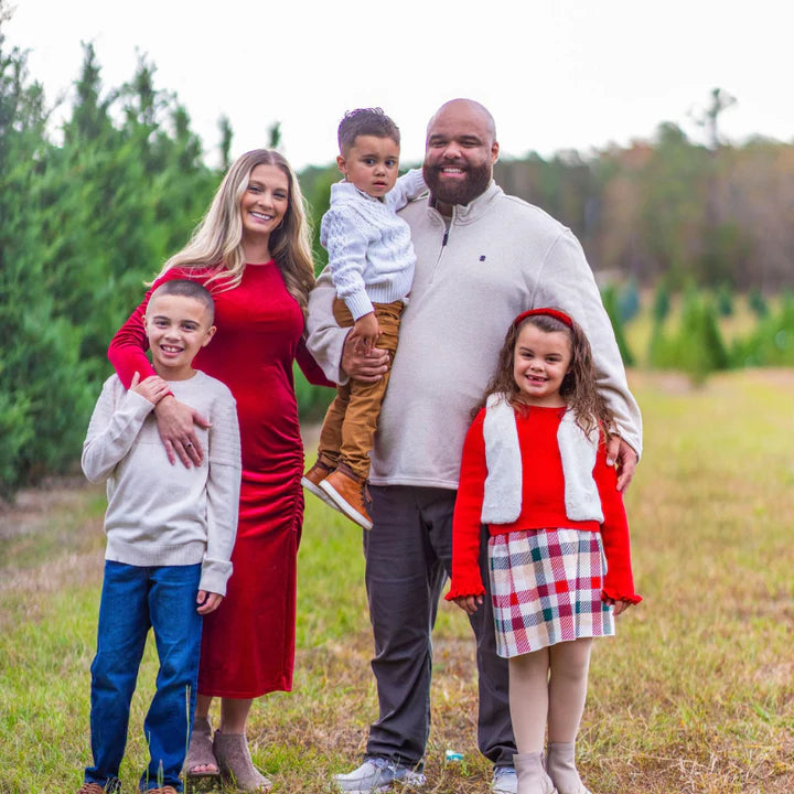 Family of five posing outdoors in a field with trees in the background