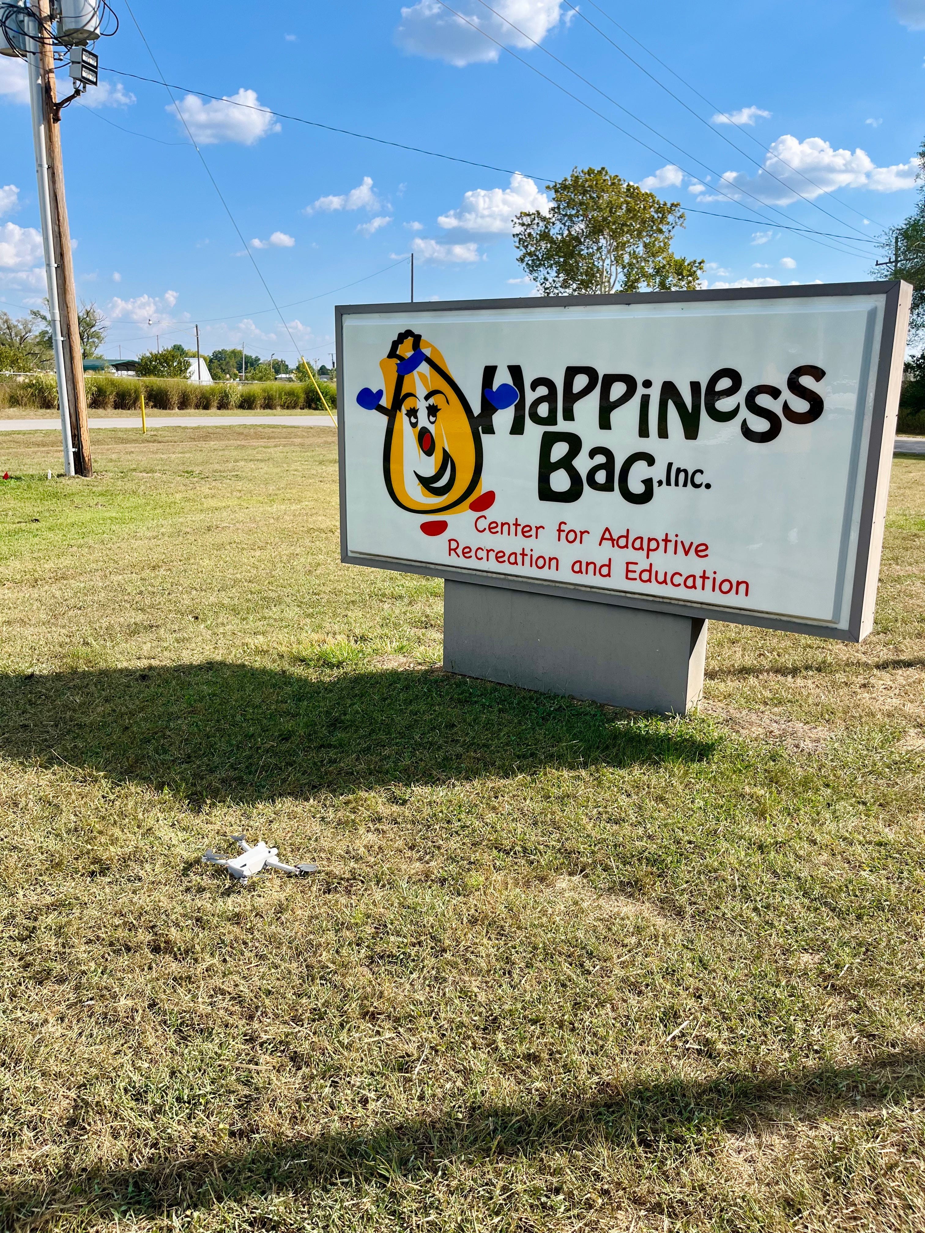 Outdoor sign for 'Happiness Bag Inc.' in a grassy area with a blue sky.