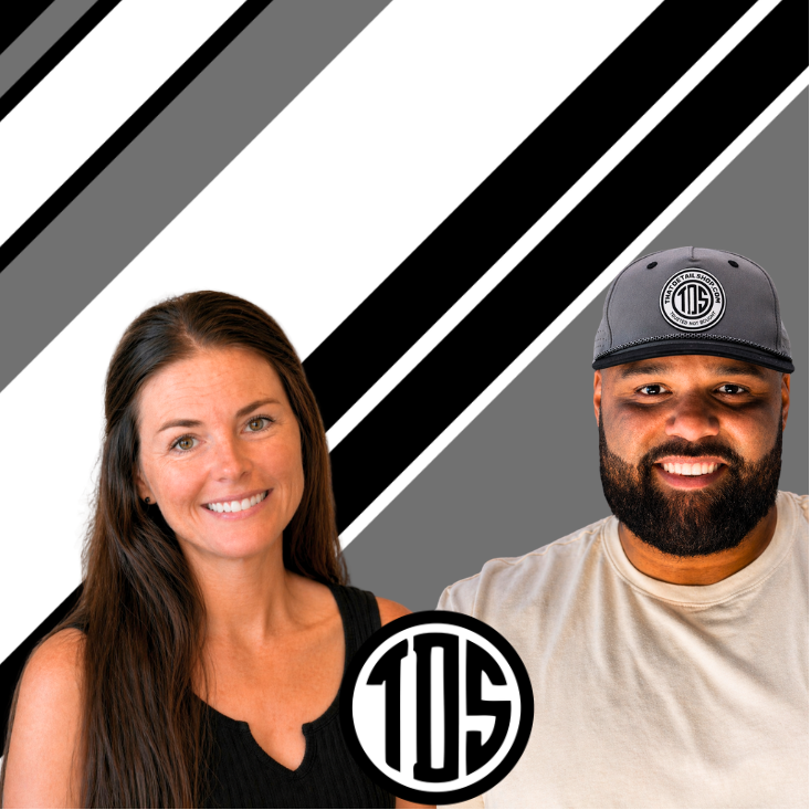Two people standing against a black, white, and gray striped background with a logo in the center.