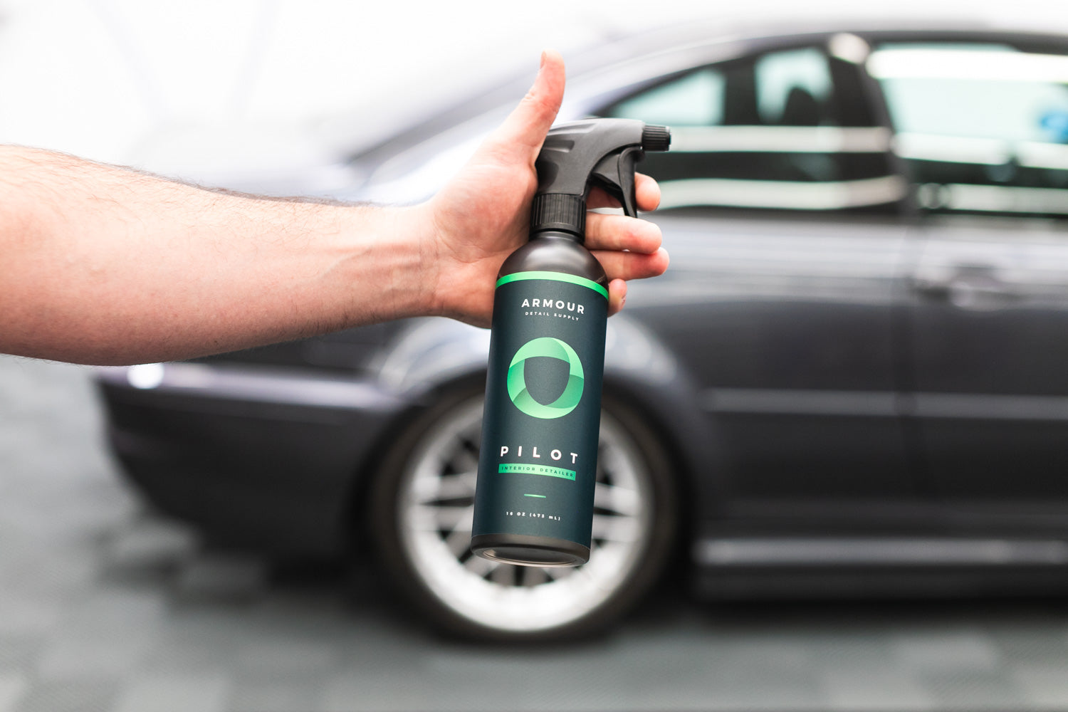 Armour Detail Supply PILOT Interior Detailer bottle held beside a car.