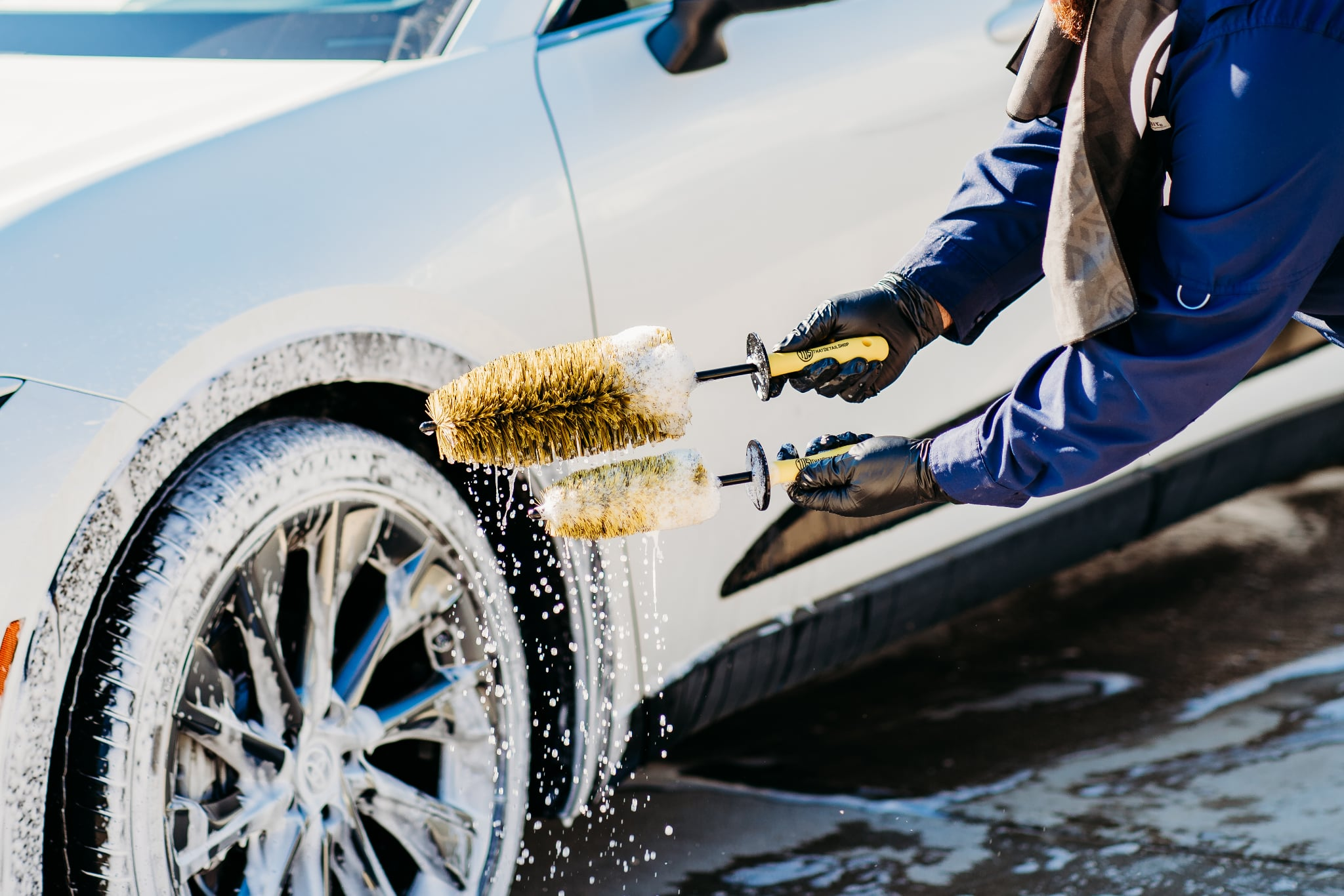 TDS long and mini barrel brushes shown in use together, held with foam-covered yellow and black bristles beside a soapy car wheel.