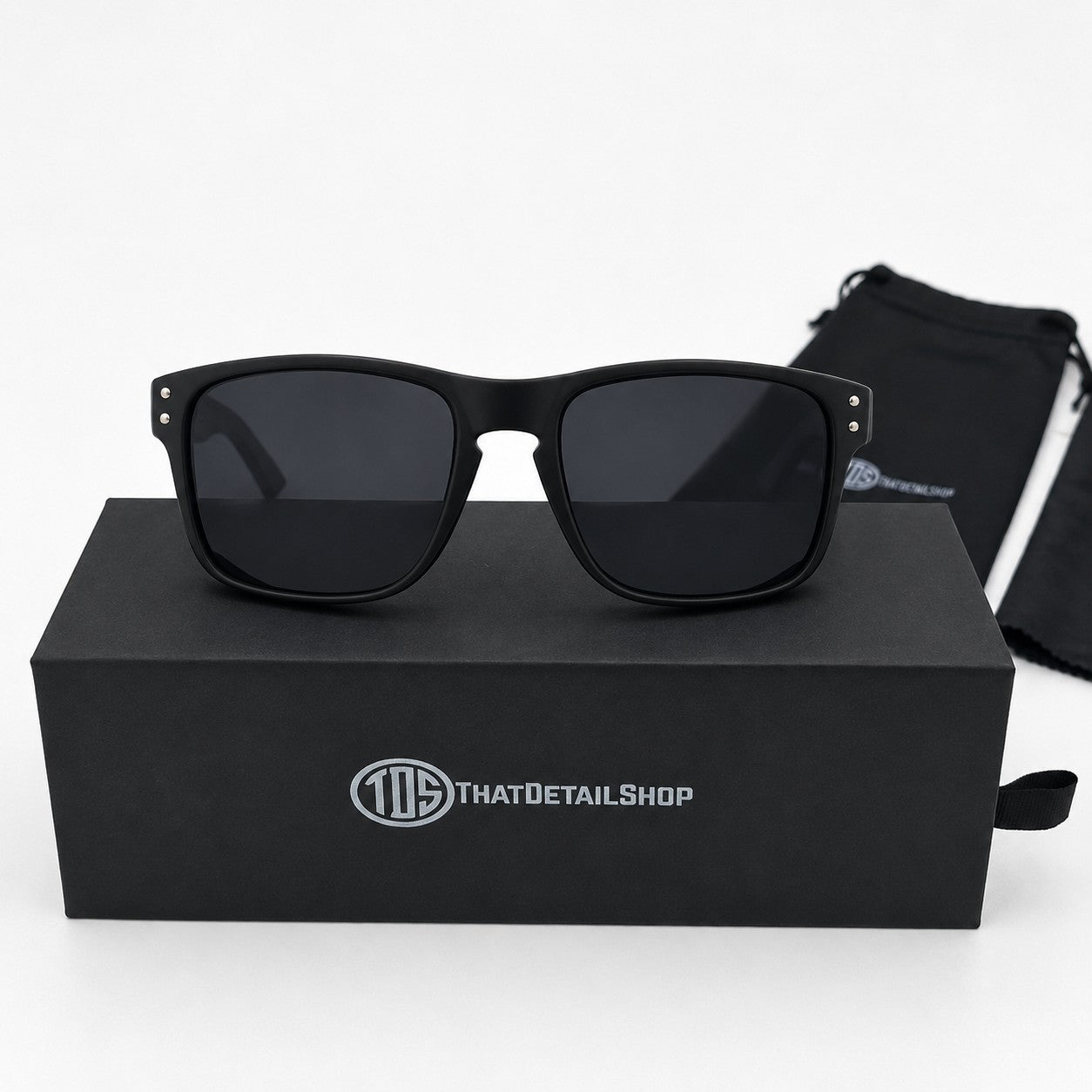 That Detail Shop polarized sunglasses in matte black with a square frame, displayed on their branded storage box.