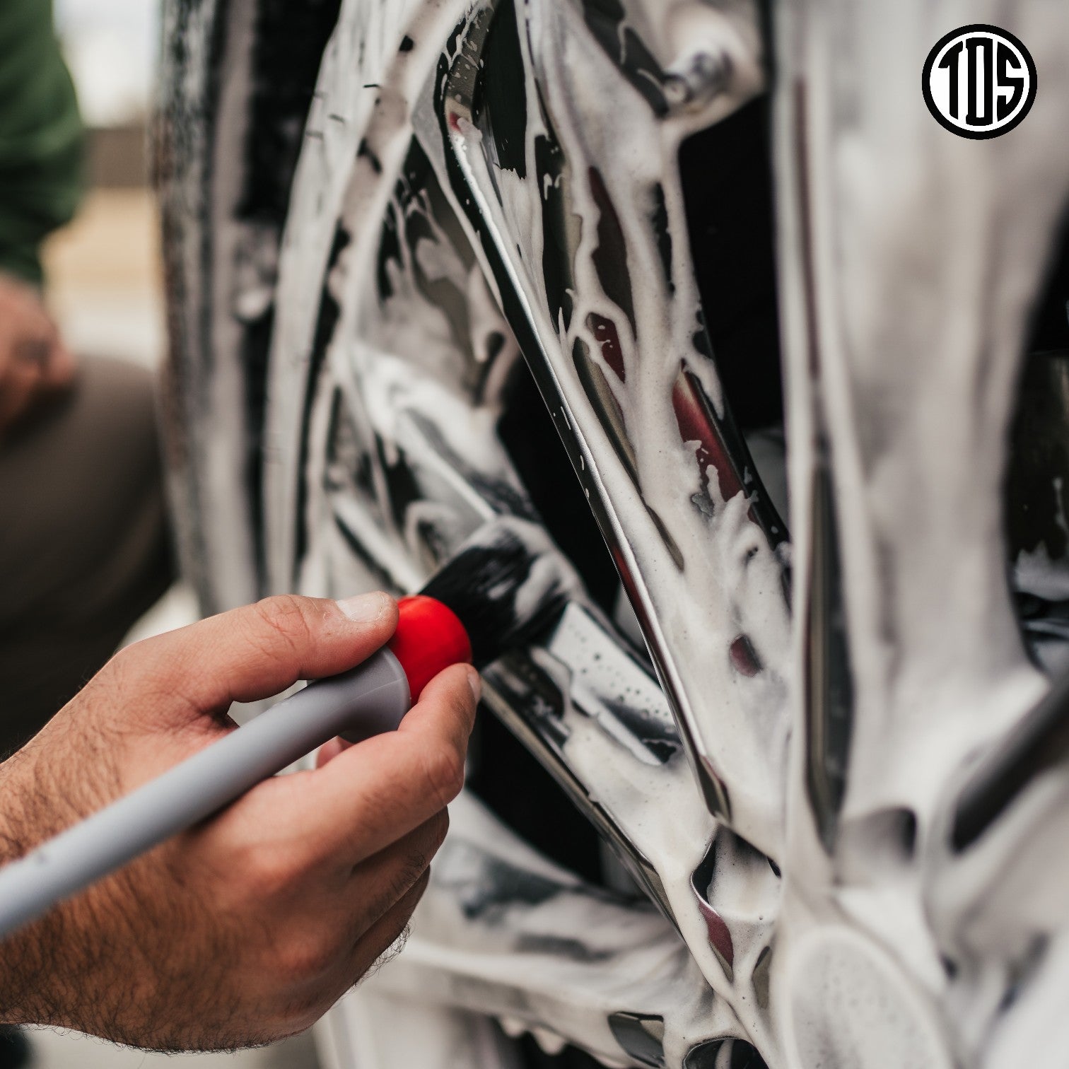 That Detail Shop exterior brush cleaning a black car wheel with foam.