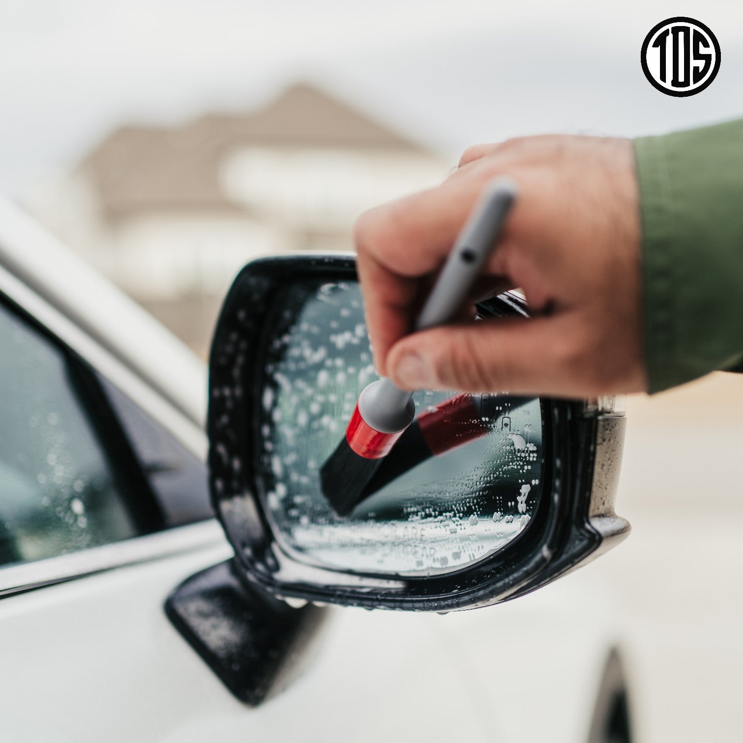 That Detail Shop exterior cleaning brush with red bristles cleaning a wet car mirror.