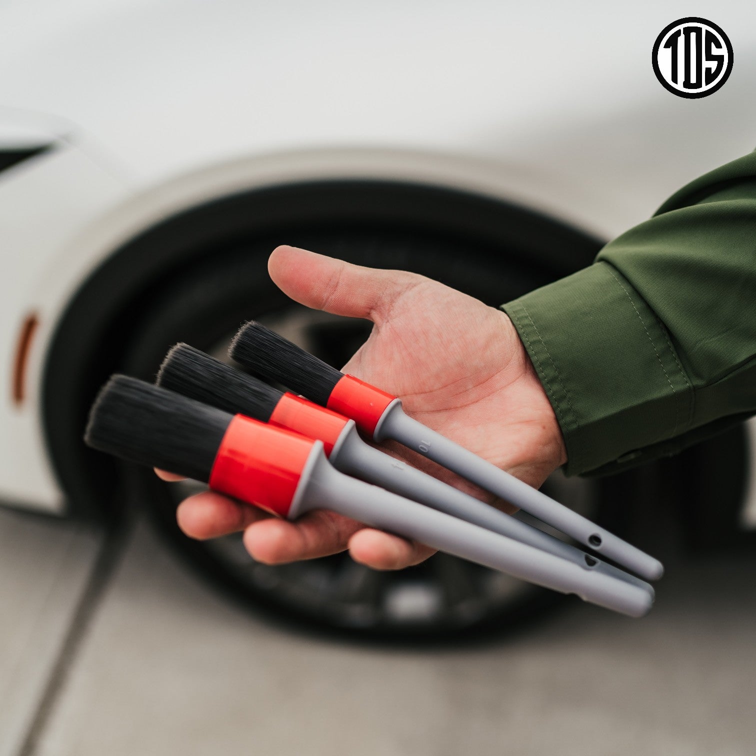 That Detail Shop exterior detailing brushes with black bristles and grey/red handles held in a hand.