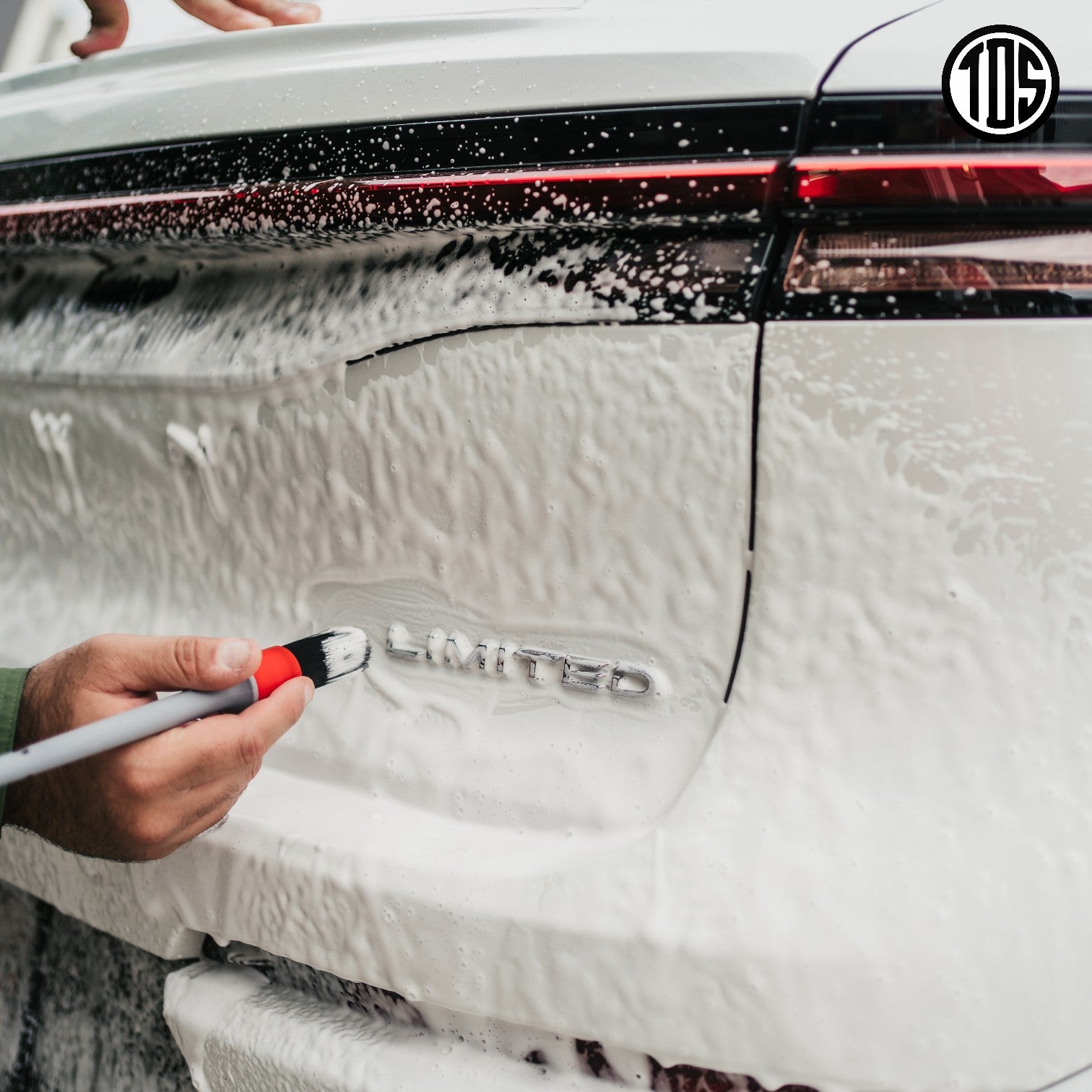That Detail Shop exterior detailing brush cleaning the 'LIMITED' emblem on a white car covered in foam.