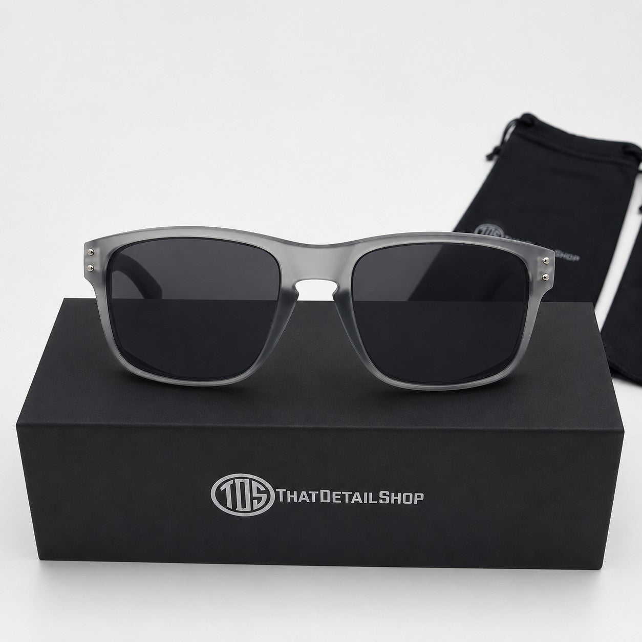 That Detail Shop polarized sunglasses with frost gray square frames and dark lenses, displayed on a branded box.