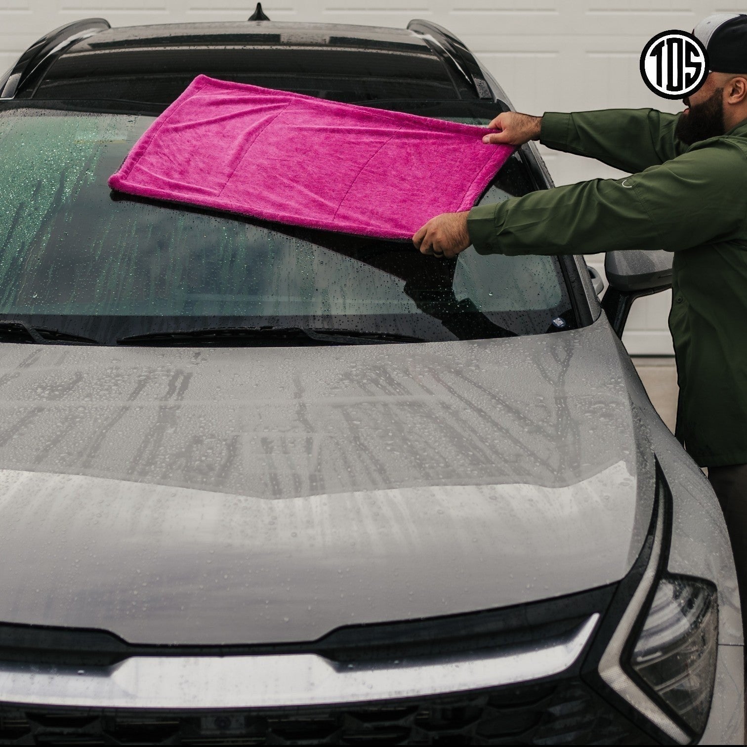 That Detail Shop pink and gray 1400 GSM microfiber drying towel being used on a wet car windshield.