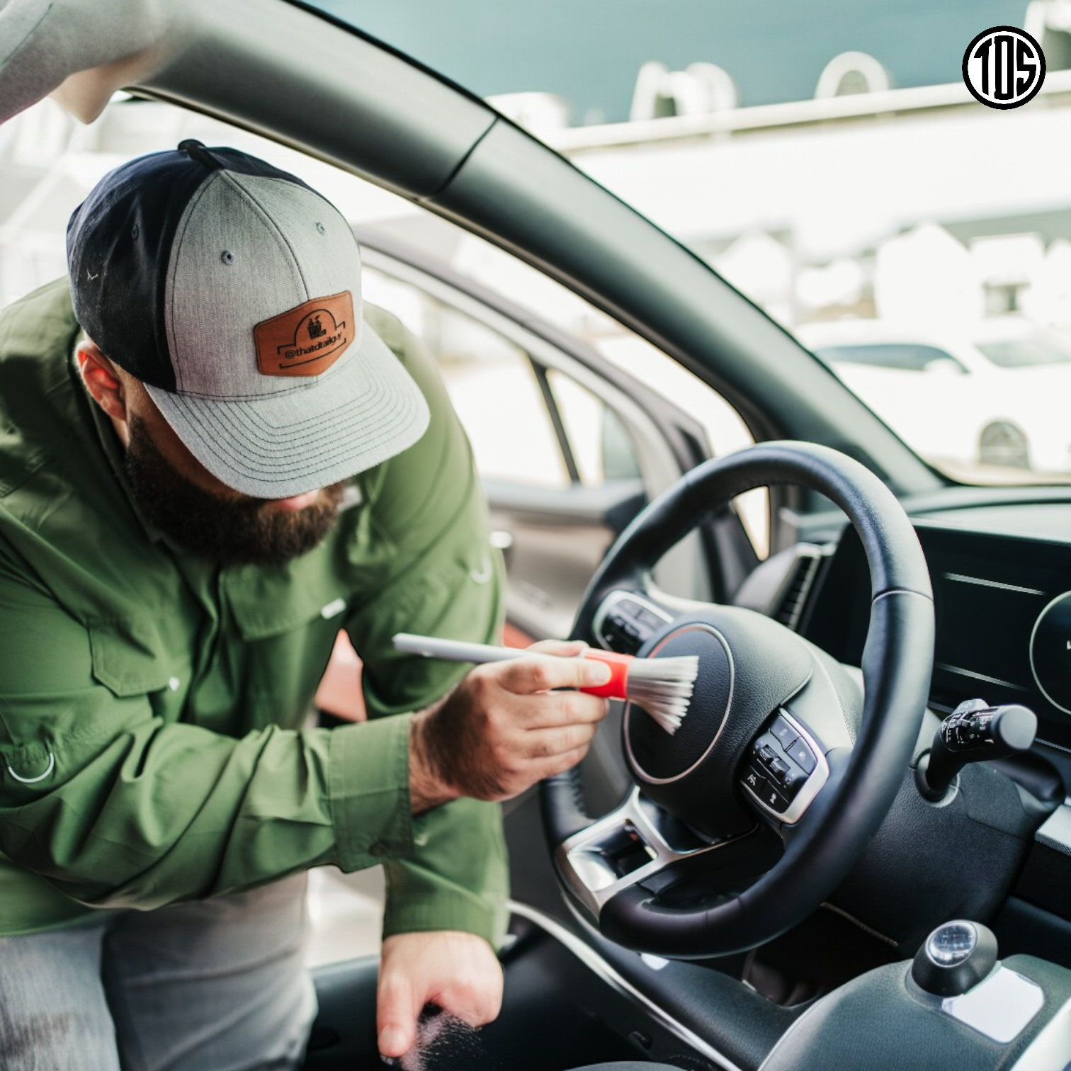 That Detail Shop interior detailing brush with red handle and soft white bristles cleaning a car steering wheel.
